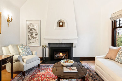 Example of a mid-sized classic formal and enclosed medium tone wood floor, brown floor and vaulted ceiling living room design in Seattle with white walls, a standard fireplace, a plaster fireplace and no tv