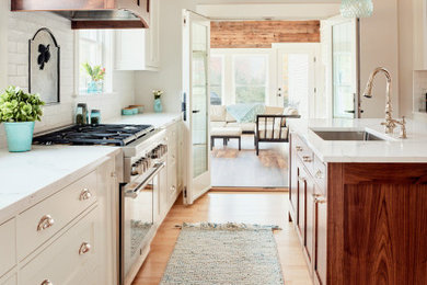 Eat-in kitchen - large cottage light wood floor eat-in kitchen idea in Portland Maine with a single-bowl sink, shaker cabinets, white cabinets, quartz countertops, white backsplash, ceramic backsplash, stainless steel appliances, an island and white countertops