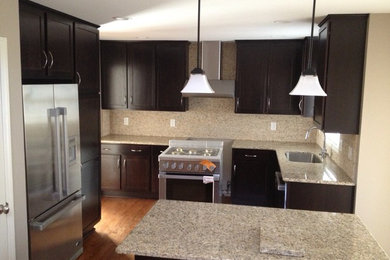 Inspiration for a mid-sized transitional l-shaped medium tone wood floor kitchen remodel in Raleigh with an undermount sink, shaker cabinets, dark wood cabinets, granite countertops, beige backsplash, stone slab backsplash and stainless steel appliances