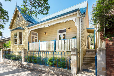 Photo of an arts and crafts two-storey yellow house exterior in Sydney with wood siding and a metal roof.