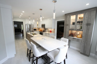 Large minimalist l-shaped porcelain tile and gray floor eat-in kitchen photo in Toronto with an undermount sink, flat-panel cabinets, white cabinets, quartz countertops, beige backsplash, mosaic tile backsplash, stainless steel appliances, an island and white countertops