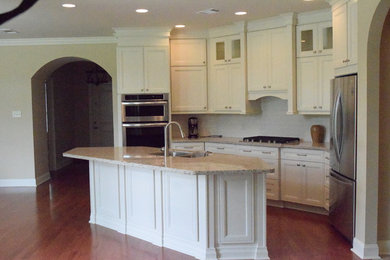 Eat-in kitchen - mid-sized transitional l-shaped light wood floor and brown floor eat-in kitchen idea in New Orleans with a double-bowl sink, glass-front cabinets, white cabinets, marble countertops, white backsplash, porcelain backsplash, stainless steel appliances and an island