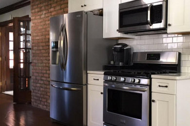 Inspiration for a mid-sized country l-shaped medium tone wood floor kitchen remodel in Cleveland with a farmhouse sink, shaker cabinets, white cabinets, white backsplash, subway tile backsplash, stainless steel appliances and a peninsula