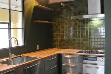 This is an example of an industrial l-shaped separate kitchen in Osaka with a drop-in sink, flat-panel cabinets, stainless steel cabinets, wood benchtops, green splashback, stainless steel appliances and no island.