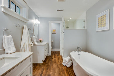Photo of a mid-sized traditional master bathroom in Other with shaker cabinets, white cabinets, a freestanding tub, an alcove shower, a two-piece toilet, grey walls, medium hardwood floors, an undermount sink, marble benchtops, a hinged shower door and brown floor.