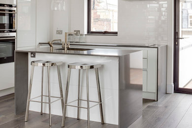 Inspiration for a contemporary kitchen in London with an undermount sink, flat-panel cabinets, white cabinets, stainless steel benchtops, white splashback, medium hardwood floors and with island.