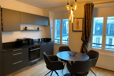 Exemple d'une cuisine ouverte linéaire et encastrable de taille moyenne avec un évier encastré, des portes de placard noires, une crédence noire, un sol en bois brun, un sol marron et plan de travail noir.