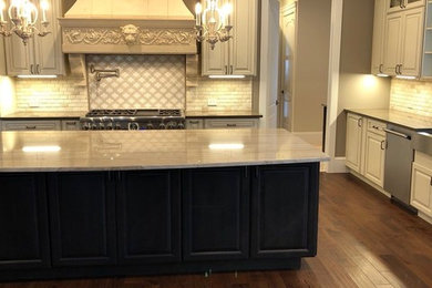 Example of a tuscan medium tone wood floor and brown floor kitchen design in DC Metro with a farmhouse sink, raised-panel cabinets, beige cabinets, granite countertops, beige backsplash, stone tile backsplash and stainless steel appliances