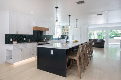 Example of a large transitional l-shaped light wood floor and multicolored floor kitchen design in Los Angeles with a farmhouse sink, shaker cabinets, white cabinets, quartz countertops, green backsplash, subway tile backsplash, paneled appliances, an island and white countertops