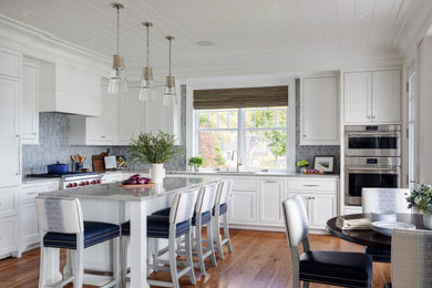 Example of a large beach style l-shaped medium tone wood floor, brown floor and shiplap ceiling open concept kitchen design in Portland Maine with an undermount sink, white cabinets, quartzite countertops, gray backsplash, stone tile backsplash, paneled appliances, an island and gray countertops