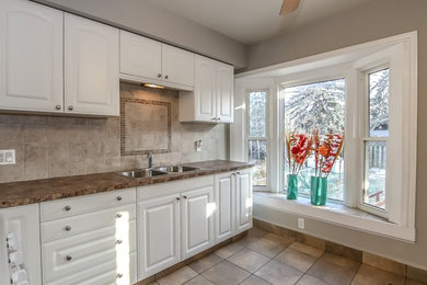 Example of a mid-sized transitional single-wall porcelain tile enclosed kitchen design in Toronto with a double-bowl sink, raised-panel cabinets, white cabinets, granite countertops, beige backsplash, stone tile backsplash and no island