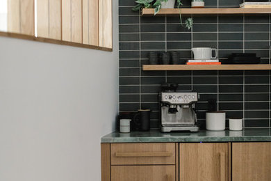 Inspiration for a mid-sized modern single-wall concrete floor and gray floor eat-in kitchen remodel in Los Angeles with an undermount sink, flat-panel cabinets, medium tone wood cabinets, limestone countertops, black backsplash, subway tile backsplash, paneled appliances, no island and green countertops