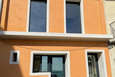 Exemple d'une façade de maison de ville orange méditerranéenne de taille moyenne et à deux étages et plus avec un toit à deux pans, un toit en tuile et un toit marron.