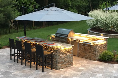 Example of a large transitional backyard stone patio kitchen design in New York with no cover
