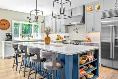 Example of a transitional l-shaped light wood floor and brown floor eat-in kitchen design in DC Metro with a drop-in sink, shaker cabinets, white cabinets, quartz countertops, white backsplash, ceramic backsplash, stainless steel appliances, an island and white countertops