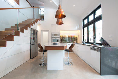 Mid-sized modern u-shaped open plan kitchen in Sydney with an undermount sink, flat-panel cabinets, white cabinets, granite benchtops, green splashback, glass sheet splashback, stainless steel appliances, concrete floors and with island.