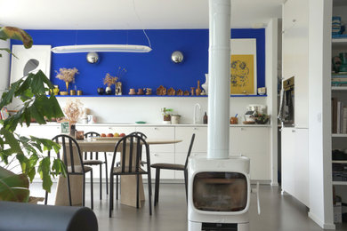 Inspiration pour une salle à manger ouverte sur le salon design de taille moyenne avec un mur bleu, sol en béton ciré, un poêle à bois et un sol gris.