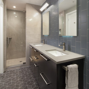 Réalisation d'une salle de bain design de taille moyenne avec un placard à porte plane, des portes de placard noires, un WC à poser, un carrelage gris, un carrelage métro, un sol en vinyl, un lavabo encastré, un mur gris et un plan de toilette en surface solide.