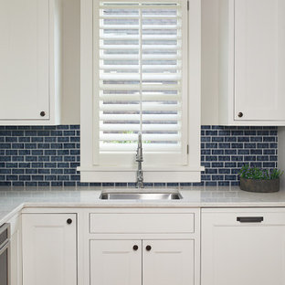 This is an example of a small beach style l-shaped kitchen pantry in Grand Rapids with an undermount sink, recessed-panel cabinets, white cabinets, blue splashback, ceramic splashback, stainless steel appliances, medium hardwood floors, no island, brown floor, white benchtop and quartz benchtops.