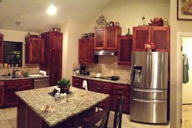 Large trendy l-shaped travertine floor eat-in kitchen photo in Austin with an undermount sink, shaker cabinets, red cabinets, granite countertops, beige backsplash, stone tile backsplash, stainless steel appliances and an island