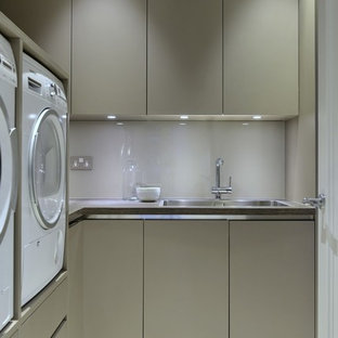 Inspiration for a medium sized contemporary u-shaped utility room in London with a submerged sink, flat-panel cabinets, composite countertops, beige walls, porcelain flooring, a side by side washer and dryer and grey cabinets.