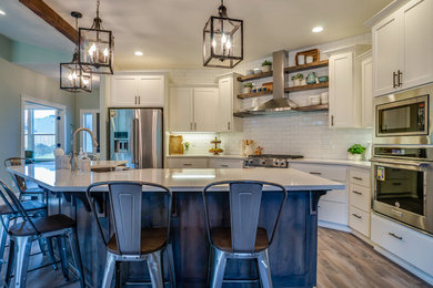 Inspiration for a brown floor open concept kitchen remodel in Portland with a farmhouse sink, shaker cabinets, white cabinets, white backsplash, subway tile backsplash, stainless steel appliances, an island and white countertops