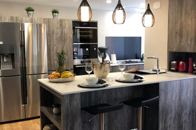 Large tropical galley open plan kitchen in Other with a drop-in sink, flat-panel cabinets, dark wood cabinets, quartz benchtops, black splashback, stainless steel appliances, porcelain floors, a peninsula, brown floor and white benchtop.