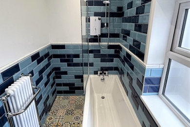 Photo of a medium sized classic family bathroom in Other with shaker cabinets, blue cabinets, a freestanding bath, a shower/bath combination, a one-piece toilet, blue tiles, porcelain tiles, white walls, porcelain flooring, a submerged sink, quartz worktops, multi-coloured floors, white worktops, a single sink and a freestanding vanity unit.