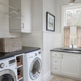 Ejemplo de cuarto de lavado costero con fregadero bajoencimera, armarios con rebordes decorativos, puertas de armario blancas, lavadora y secadora juntas, suelo gris y encimeras negras