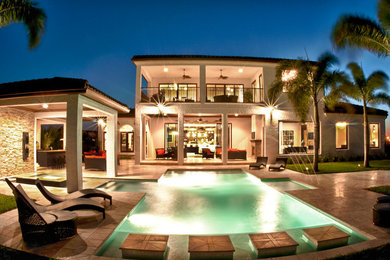 Design ideas for a large contemporary backyard custom-shaped pool in Orlando with a hot tub and natural stone pavers.