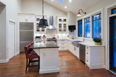 Beach style l-shaped open plan kitchen in Calgary with a farmhouse sink, shaker cabinets, white cabinets, quartzite benchtops, white splashback, subway tile splashback, stainless steel appliances, dark hardwood floors, with island and brown floor.