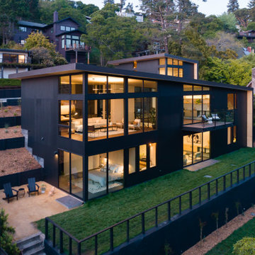 Modern hillside home exterior at dusk - angular roofline, floor-to-ceiling glazi