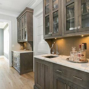 チャールストンの大きいビーチスタイルのおしゃれなウェットバー (淡色無垢フローリング、アンダーカウンターシンク、落し込みパネル扉のキャビネット、濃色木目調キャビネット、珪岩カウンター、茶色いキッチンパネル) の写真