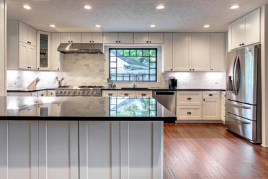 Huge transitional galley bamboo floor and brown floor open concept kitchen photo in Houston with a single-bowl sink, shaker cabinets, white cabinets, granite countertops, white backsplash, travertine backsplash, stainless steel appliances, an island and black countertops
