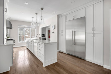Large transitional galley medium tone wood floor and brown floor eat-in kitchen photo in Detroit with an undermount sink, shaker cabinets, white cabinets, quartz countertops, white backsplash, ceramic backsplash, stainless steel appliances, an island and white countertops