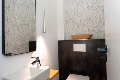 Kleines Modernes Badezimmer mit hellbraunen Holzschränken, Toilette mit Aufsatzspülkasten, Keramikboden, Waschtisch aus Holz, schwarzem Boden, Einzelwaschbecken und Tapetenwänden in Bremen
