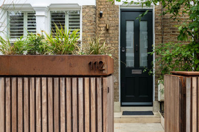 This is an example of a mid-sized contemporary three-storey brick brown townhouse exterior in London with a gable roof, a tile roof, a black roof and board and batten siding.