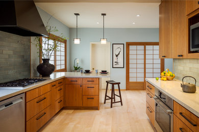 This is an example of an asian u-shaped kitchen in San Francisco with flat-panel cabinets, medium wood cabinets, green splashback, subway tile splashback, stainless steel appliances, light hardwood floors, a peninsula, beige floor and beige benchtop.