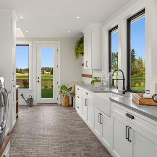 Photo of an expansive farmhouse l-shaped utility room in Portland with a belfast sink, shaker cabinets, white cabinets, engineered stone countertops, white walls, ceramic flooring, a side by side washer and dryer, grey floors and grey worktops.