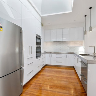 Inspiration pour une grande arrière-cuisine minimaliste en U avec un évier 2 bacs, des portes de placard blanches, un plan de travail en inox, une crédence grise, une crédence en carreau de céramique, un électroménager noir, un sol en bois brun, aucun îlot, un sol orange et un plan de travail blanc.