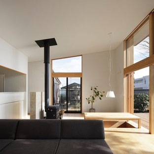 Exemple d'une grande salle à manger ouverte sur le salon asiatique avec un mur blanc, un sol en contreplaqué, un poêle à bois, un manteau de cheminée en carrelage et un sol beige.