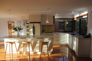 Mid-sized traditional galley open plan kitchen in Melbourne with a double-bowl sink, flat-panel cabinets, white cabinets, quartz benchtops, beige splashback, glass sheet splashback, stainless steel appliances, cork floors, with island and brown floor.