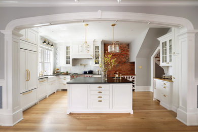 Eat-in kitchen - traditional l-shaped eat-in kitchen idea in Wilmington with a farmhouse sink, white cabinets, soapstone countertops, white backsplash, paneled appliances, an island and black countertops