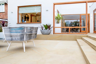 This is an example of a medium sized contemporary back patio in Hertfordshire with natural stone paving.