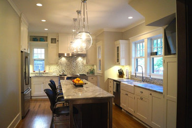 Example of a mid-sized arts and crafts l-shaped medium tone wood floor eat-in kitchen design in Cedar Rapids with a farmhouse sink, flat-panel cabinets, white cabinets, granite countertops, multicolored backsplash, glass tile backsplash, stainless steel appliances and an island