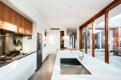 Photo of a large contemporary galley eat-in kitchen in Sydney with a drop-in sink, flat-panel cabinets, white cabinets, quartz benchtops, metallic splashback, metal splashback, stainless steel appliances, concrete floors, with island, grey floor and white benchtop.