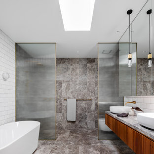 Photo of a mid-sized industrial master bathroom in Sydney with glass-front cabinets, a freestanding tub, an open shower, a wall-mount toilet, black tile, subway tile, limestone floors, an integrated sink, limestone benchtops, grey floor, an open shower, a double vanity and a built-in vanity.