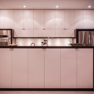 Cette photo montre une arrière-cuisine parallèle moderne de taille moyenne avec un évier 2 bacs, un placard à porte plane, des portes de placard blanches, un plan de travail en granite, une crédence grise, un électroménager en acier inoxydable, un sol en carrelage de céramique et un îlot central.