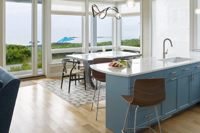 Example of a beach style medium tone wood floor eat-in kitchen design in Portland Maine with an undermount sink, shaker cabinets, blue cabinets, marble countertops and white countertops