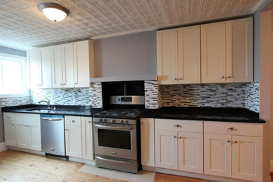 Open concept kitchen - mid-sized contemporary single-wall light wood floor and beige floor open concept kitchen idea in New York with an undermount sink, shaker cabinets, white cabinets, granite countertops, multicolored backsplash, matchstick tile backsplash, stainless steel appliances and no island